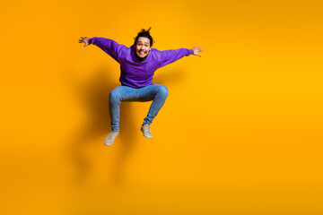 Obraz premium Vibrant young man in casual purple sportswear mid-jump against a bright yellow background showcasing energy and style