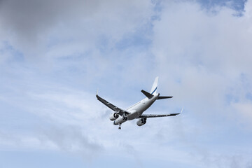 Commercial airplane flying in cloudy blue sky with landing gear down preparing for arrival at airport