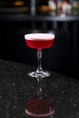 Classic clover club raspberry gin alcoholic cocktail in dark bar atmosphere with bokeh lights
