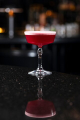 Classic clover club raspberry gin alcoholic cocktail in dark bar atmosphere with bokeh lights
