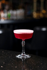 Classic clover club raspberry gin alcoholic cocktail in dark bar atmosphere with bokeh lights
