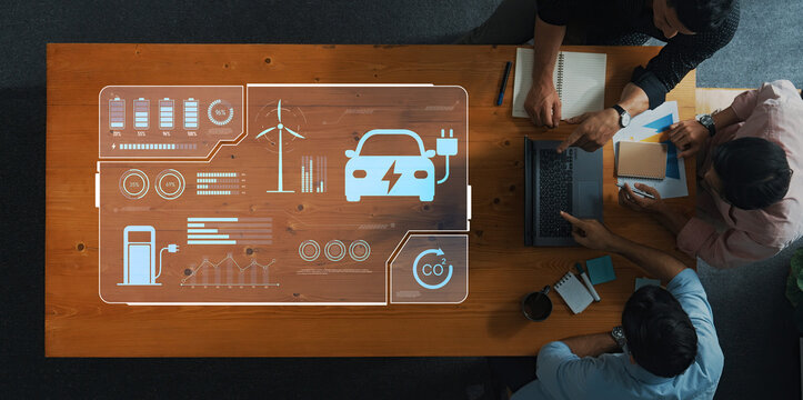 Team members engage in a brainstorming session, discussing electric vehicle technology and renewable energy strategies, highlighting data and innovative ideas on a wooden table. Trope