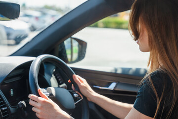 Naklejka premium Woman driving a car in a sunny parking lot with focus on steering wheel