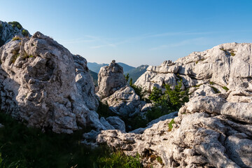 Impressive white karst rock formations frame a scenic mountain vista under a clear blue summer sky in the majestic Velebit mountains, a popular hiking destination near the Adriatic coast of Croatia.