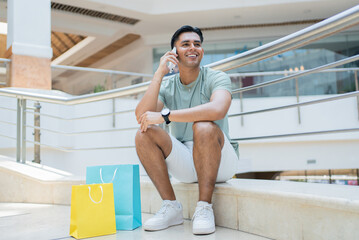 Obraz premium Smiling young man sitting in a mexican shopping mall making a phone call
