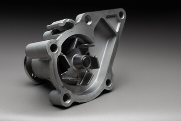 A new, shiny aluminum engine coolant pump on a gray gradient background. Contrast backlighting.