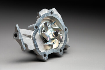 Top-quality parts for your car. Car maintenance. New water pump for a car's engine cooling system on a gray gradient background.