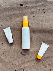 Sunblock bottles on the sand. Top view. A white plastic spray bottle with a yellow cap .Minimalist beach-themed composition, suitable for concepts of summer, skincare, sunscreen