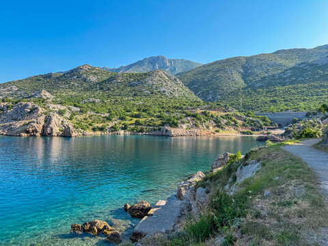 A secluded, picturesque bay with calm, turquoise waters is nestled at the foot of the green Velebit mountains along the Adriatic coast, offering a tranquil and idyllic scene in Karlobag, Croatia.