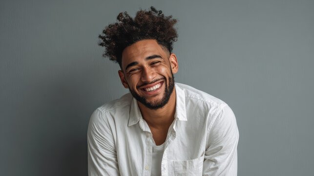 horizontal shot of happy mixed race male with shining smile feels glad as recieves bonus and praise for good work has specific appearance afro hairstyle dressed in fashionable white shirt no logos no - Powered by Adobe