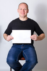 Happy bald man sitting holding horizontal blank white paper sign for text