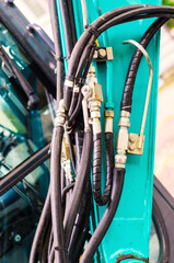 Close up of complex hydraulic hoses and metallic fittings on bright teal machinery