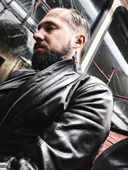 Bearded man in leather jacket resting on subway train during late evening commute