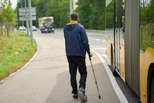 Person with injured leg walking with crutches near road Injured leg in boot, crutches, city sidewalk, bus, movement - Powered by Adobe