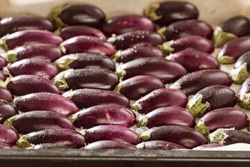 Dozens of petite, purple eggplants sit on a baking sheet. They are sprinkled with salt and ready to be roasted to make a delicious, healthy meal