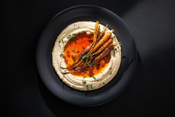 A plate holds a swirl of hummus, topped with roasted carrots and a drizzle of orange sauce. Garnished with pomegranate seeds and fresh herbs, a culinary delight