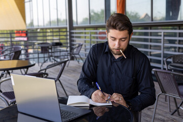 Man sitting at table, focused on laptop, writing intently