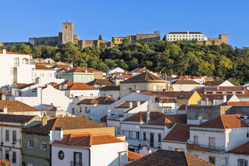 A scenic view of the Palmela Castle, perched high on a lush hill, dominating the traditional whitewashed houses with terracotta roofs below in Portugal