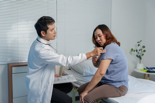 Doctor examining female patient with shoulder pain, discussing medical history in a modern clinic office. Healthcare consultation
