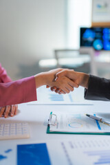 Two businesswomen confirming a business deal with a handshake over a table with reports and a calculator during an office meeting