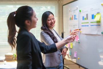 Young businesswomen collaborating on a project, analyzing data and charts on a whiteboard during a meeting in a modern office