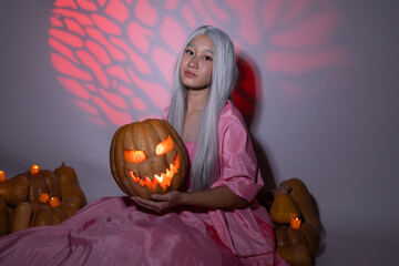 Woman in pink dress holding a pumpkin amidst colorful autumn leaves