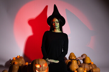 Woman in black dress and hat stands next to pile of pumpkins