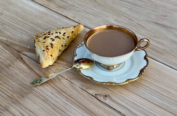 Coffee in antique coffee set with silver gold plated spoon on saucer and cheese borek on oak table. Close-up front view.