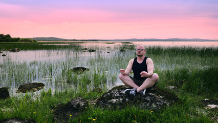 Fototapeta premium Man meditating outdoors on rocks near Galway coast Ireland, practicing mindfulness, yoga, relaxation, mental health, wellness, freedom, and nature balance