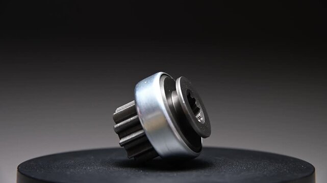 A rotating part on a gray gradient background. A starter drive is a metal part of an internal combustion engine.