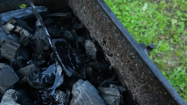 Close-up of charcoal in grill and hand pouring flammable liquid to prepare the grill for ignition