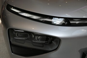 Detail of sleek elegant LED headlights and square shaped dual fog lights under, installed on modern chinese battery electric mid-size crossover SUV car. 