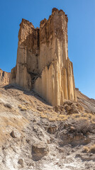 Towering golden rock formations rise dramatically against a clear blue sky, revealing the timeless beauty of desert cliffs and rugged landscapes. The warm sunlight enhances the golden tones of the sto