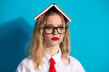 Young woman with a book on her head on a vibrant blue background