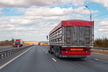 A large truck travels along a multi-lane highway under partly cloudy skies, transporting goods and...