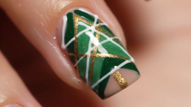 A close up shot of a fingernail featuring green nail art with white and golden stripes, showcasing modern geometric pattern and elegant design for beauty and style