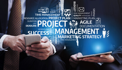 Two business professionals discuss project management while using digital devices. The image...