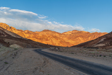 Curving Desert Road Leading to Rugged Mountains Under Blue, Partly Cloudy Sky Death Valley National Park