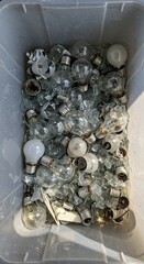 Discarded light bulbs in a plastic bin filled with glass fragments  