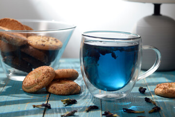 Blue butterfly pea tea in glass cup with cookies on blue wooden table