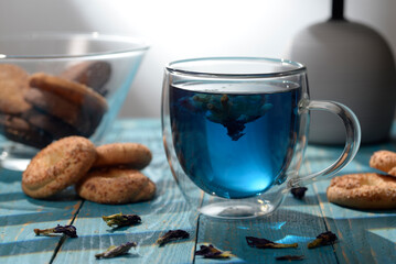 Blue butterfly pea tea in glass cup with cookies on blue wooden table