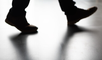 Blurred silhouette of a person's feet in boots walking on dark surface, heavily backlit, casting long, dramatic shadows