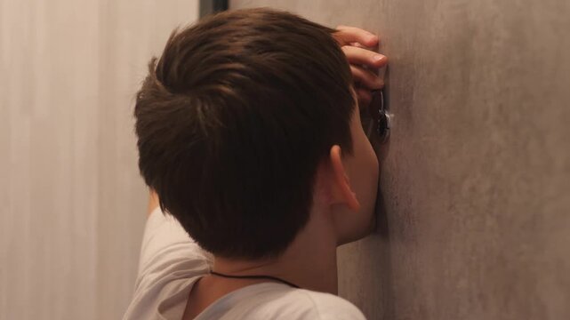 A Caucasian boy aged 10-12 years, being alone at home, looks through the peephole with apprehension, the child looks through the peephole