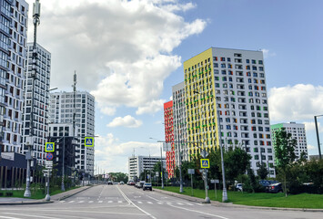 Modern residential district with tall colorful apartment buildings, wide road, green lawns, and...