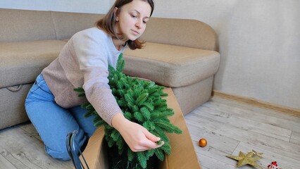 A woman takes a Christmas tree out of a box, preparing to decorate it