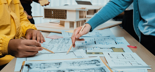 A group of professionals engages in a collaborative design session, reviewing architectural plans and sketches while brainstorming ideas in a modern office environment. SACTR