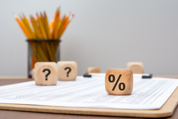 wooden cube with percent sign and question marks on financial document in office