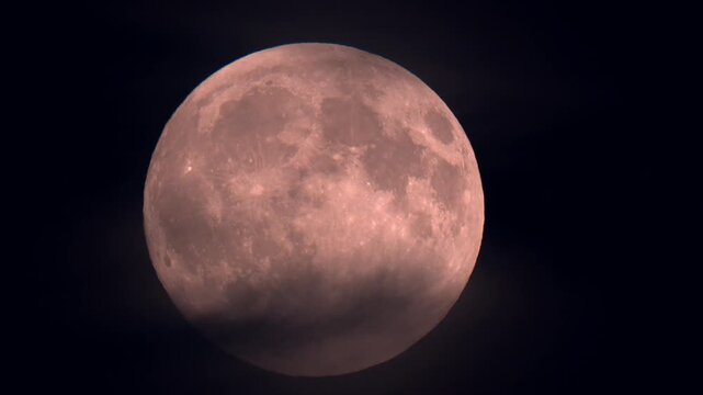 Harvest supermoon rising though clouds