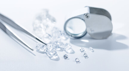 Clear diamonds with tweezers and magnifier on white background