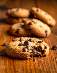 Close-up of several chocolate chip cookies, one with a bite taken out, resting on a wooden surface.  The cookies are golden brown with visible chocolate chips